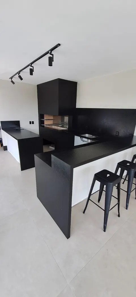 Área gourmet em granito preto com balcão, banquetas e churrasqueira
